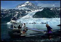 Man and woman  unload  kayak from the water taxi boat at Black Sand Beach. Prince William Sound, Alaska, USA ( color)