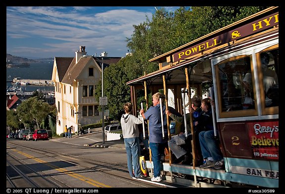 Cable car plunging with people clinging on Hyde Street, late afternoon. San Francisco, California, USA (color)
