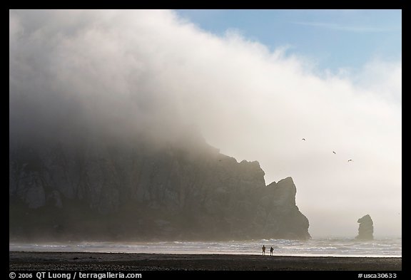 Two people strolling on the beach at the base of Morro Rock. Morro Bay, USA (color)