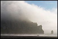Two people strolling on the beach at the base of Morro Rock. Morro Bay, USA (color)