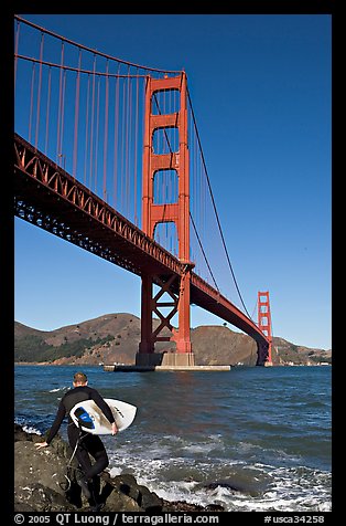 Surfer stepping on rocks and Golden Gate Bridge. San Francisco, California, USA