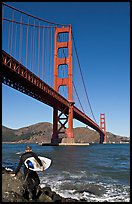 Surfer stepping on rocks and Golden Gate Bridge. San Francisco, California, USA (color)