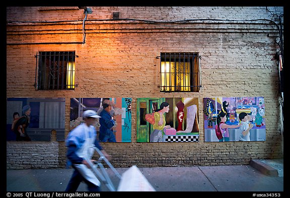 Man pushing a cart in front of mural paintings, Ross Alley, Chinatown. San Francisco, California, USA (color)