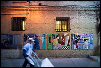 Man pushing a cart in front of mural paintings, Ross Alley, Chinatown. San Francisco, California, USA (color)