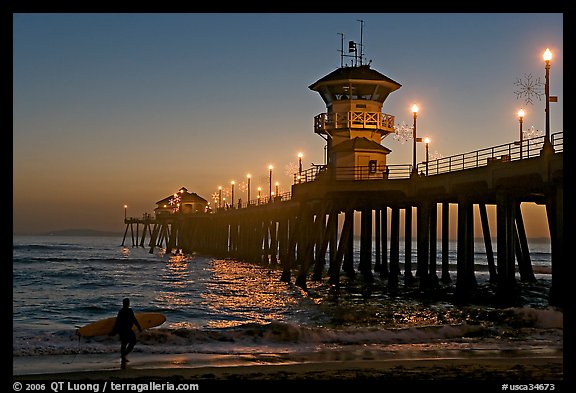 Surfer and Huntington Pier lights at twilight. Huntington Beach, Orange County, California, USA