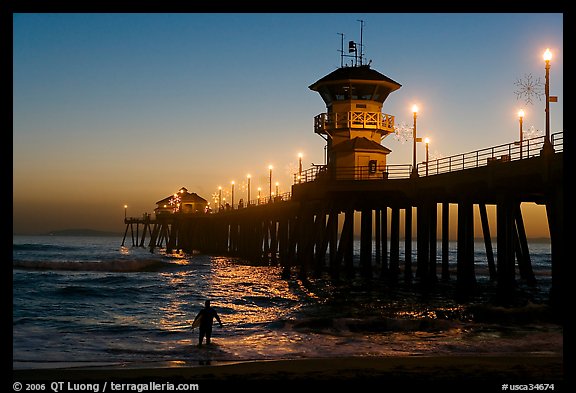 Surfer entering water next to the Huntington Pier, sunset. Huntington Beach, Orange County, California, USA