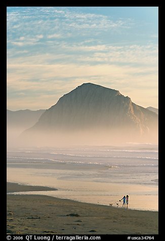 Women walking dog on the beach, with Morro Rock behind. Morro Bay, USA (color)