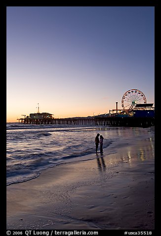 Couple standing on the beach at sunset, with pier and Ferris Wheel behind. Santa Monica, Los Angeles, California, USA (color)