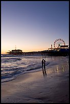 Couple standing on the beach at sunset, with pier and Ferris Wheel behind. Santa Monica, Los Angeles, California, USA