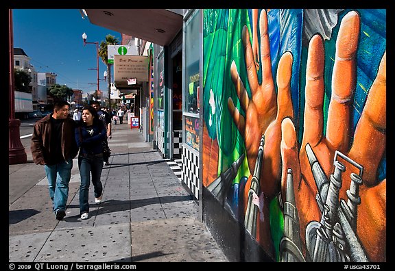 Couple walks past mural on Mission street, Mission District. San Francisco, California, USA