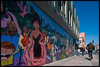 Man riding bicycle on sidewalk past mural, Mission District. San Francisco, California, USA ( color)