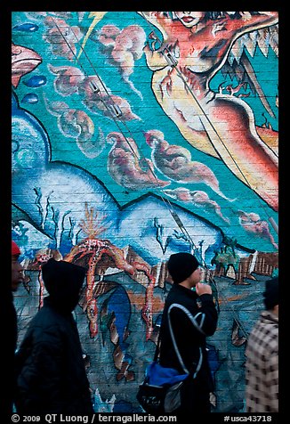 Men in dark jackets walk past mural, Mission District. San Francisco, California, USA