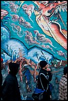 Men in dark jackets walk past mural, Mission District. San Francisco, California, USA ( color)