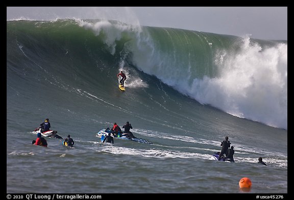 Surfer down huge wall of water observed from jet skis. Half Moon Bay, California, USA