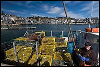 Lobsterman in boat with traps, and village in background. Stonington, Maine, USA (color)