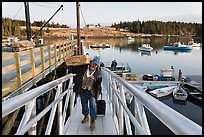 Man carrying construction wood and rolling case out of mailboat. Isle Au Haut, Maine, USA (color)