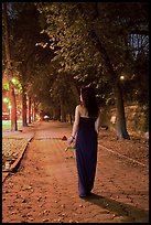 Woman in evening dress with rose on alley bordering Central Park at night. NYC, New York, USA