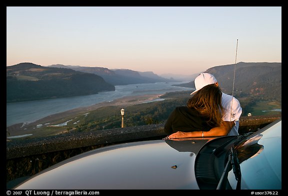 Couple embracing on car hood, with view of mouth of river gorge. Columbia River Gorge, Oregon, USA (color)