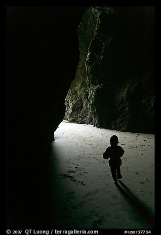 Infant walking towards the light in sea cave. Bandon, Oregon, USA (color)