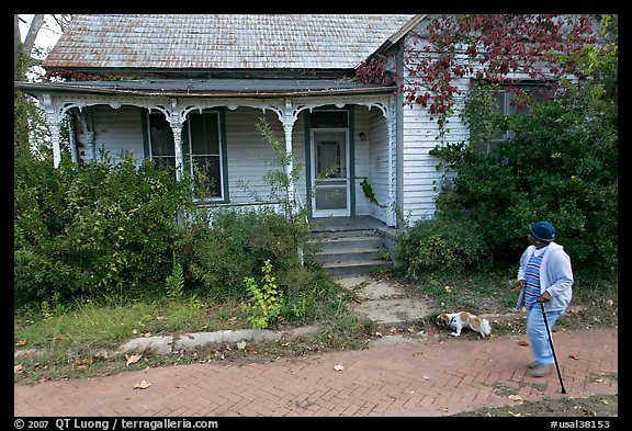 Woman walking dog in front of a crooked house. Selma, Alabama, USA