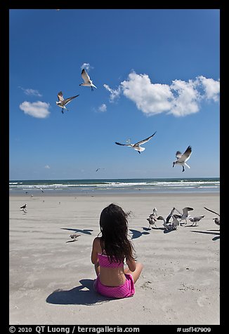 Girl sitting on beach with birds flying, Jetty Park. Cape Canaveral, Florida, USA (color)