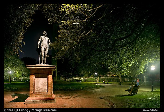 Park with statue and couples sitting on public benches at night. Charleston, South Carolina, USA