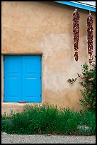Ristras hanging from roof with blue shutters. Taos, New Mexico, USA