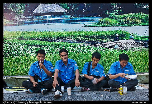 Uniformed students eating in front of backdrop depicting rural landscape. Ho Chi Minh City, Vietnam