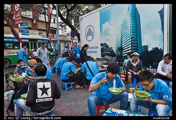 Uniformed students eating breakfast in front of backdrop depicting high rise in construction. Ho Chi Minh City, Vietnam