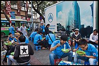 Uniformed students eating breakfast in front of backdrop depicting high rise in construction. Ho Chi Minh City, Vietnam ( color)