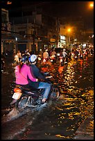 Couple riding motorcycle on flooded street at night. Ho Chi Minh City, Vietnam
