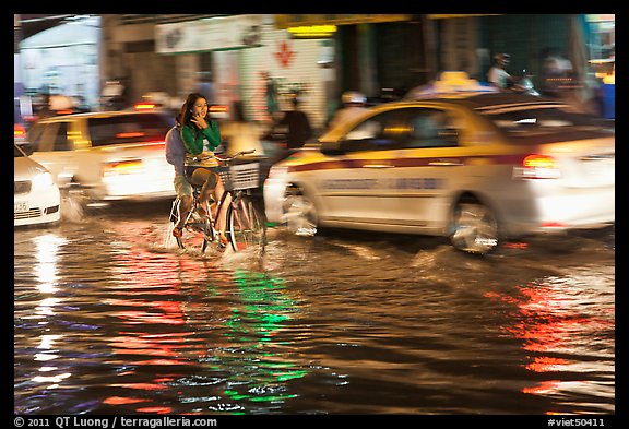 Women riding a bicycle on a flooded street at night. Ho Chi Minh City, Vietnam