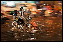 Girls sharing night bicycle ride through water of flooded street. Ho Chi Minh City, Vietnam ( color)