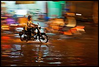 Motorcyclist speeding on wet street at night, with streaks giving sense of motion. Ho Chi Minh City, Vietnam (color)
