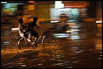 Men sharing bicycle ride at night on wet street. Ho Chi Minh City, Vietnam ( color)