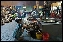 Woman feeding furnace in cococut candy factory. Ben Tre, Vietnam (color)