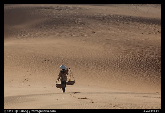Woman walking on dune field with yoke baskets. Mui Ne, Vietnam (color)