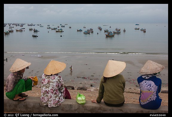 Four women in conical hats watch fishing activity from high above fishing village. Mui Ne, Vietnam