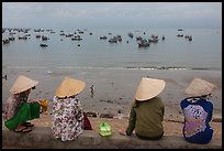 Four women in conical hats watch fishing activity from high above fishing village. Mui Ne, Vietnam (color)