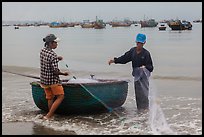 Man and woman gathering fishing net onto roundboat. Mui Ne, Vietnam (color)