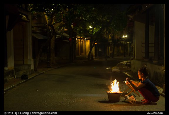 Woman burning paper on street at night. Hoi An, Vietnam
