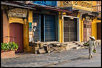 Woman carrying fruit in front of old storefronts. Hoi An, Vietnam (color)