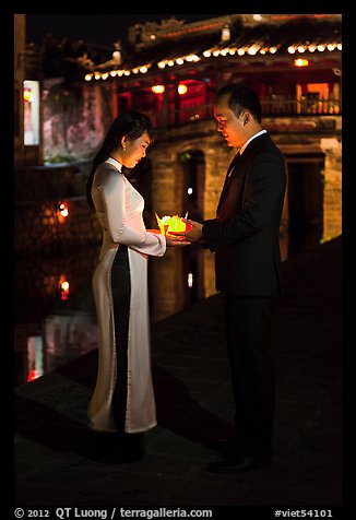 Couple holding candles in front of Japanese bridge at night. Hoi An, Vietnam