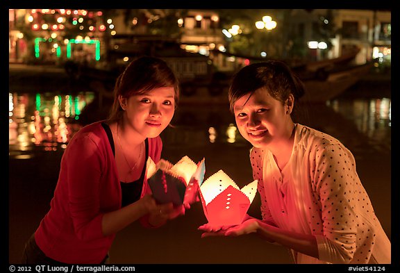 Two women lighted by candle box at night. Hoi An, Vietnam