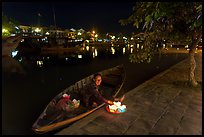 Woman sitting in rowboat selling candles on quay. Hoi An, Vietnam ( color)