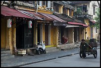 Man pulling cart in front of old townhouses. Hoi An, Vietnam (color)