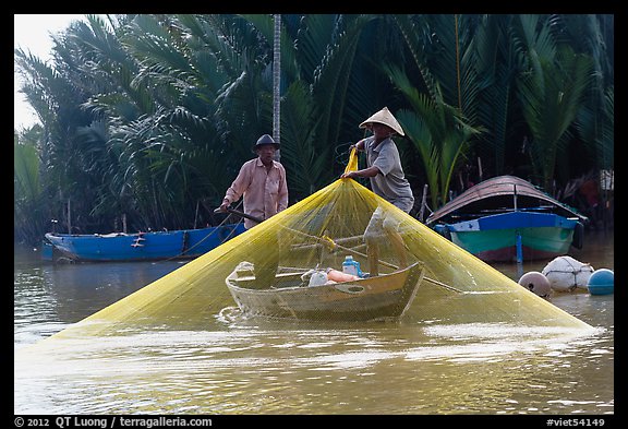 Fisherman pulls up net from rowboat. Hoi An, Vietnam