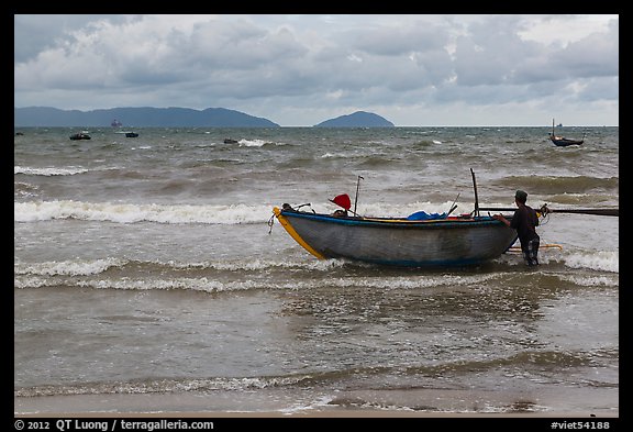 Man entering ocean with boat in stormy weather. Da Nang, Vietnam