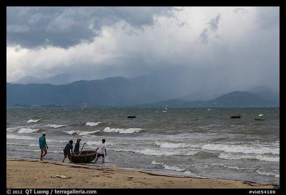 Men pushing coracle boat into stormy ocean. Da Nang, Vietnam (color)