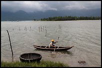 Fisherman rowing canoe in lagoon. Vietnam (color)